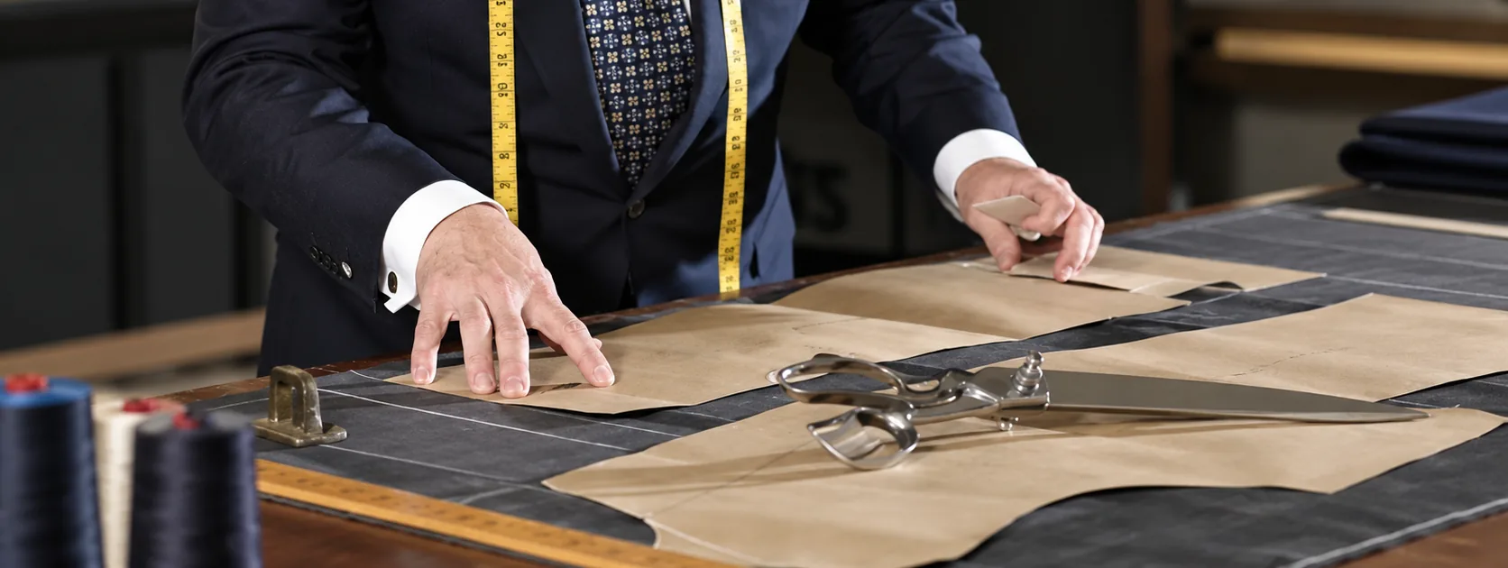 A tailor laying out pattern pieces on the cutting table beside a pair of shears