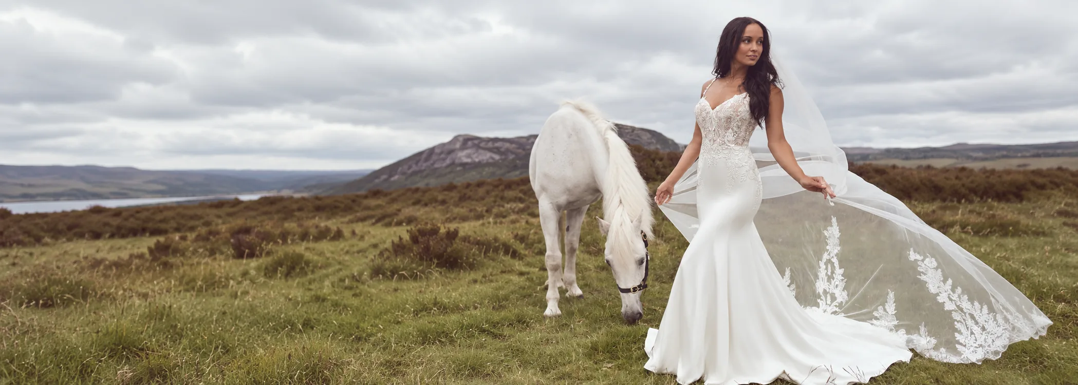 A bride in a fitted lace and crepe wedding gown with a long embroidered veil