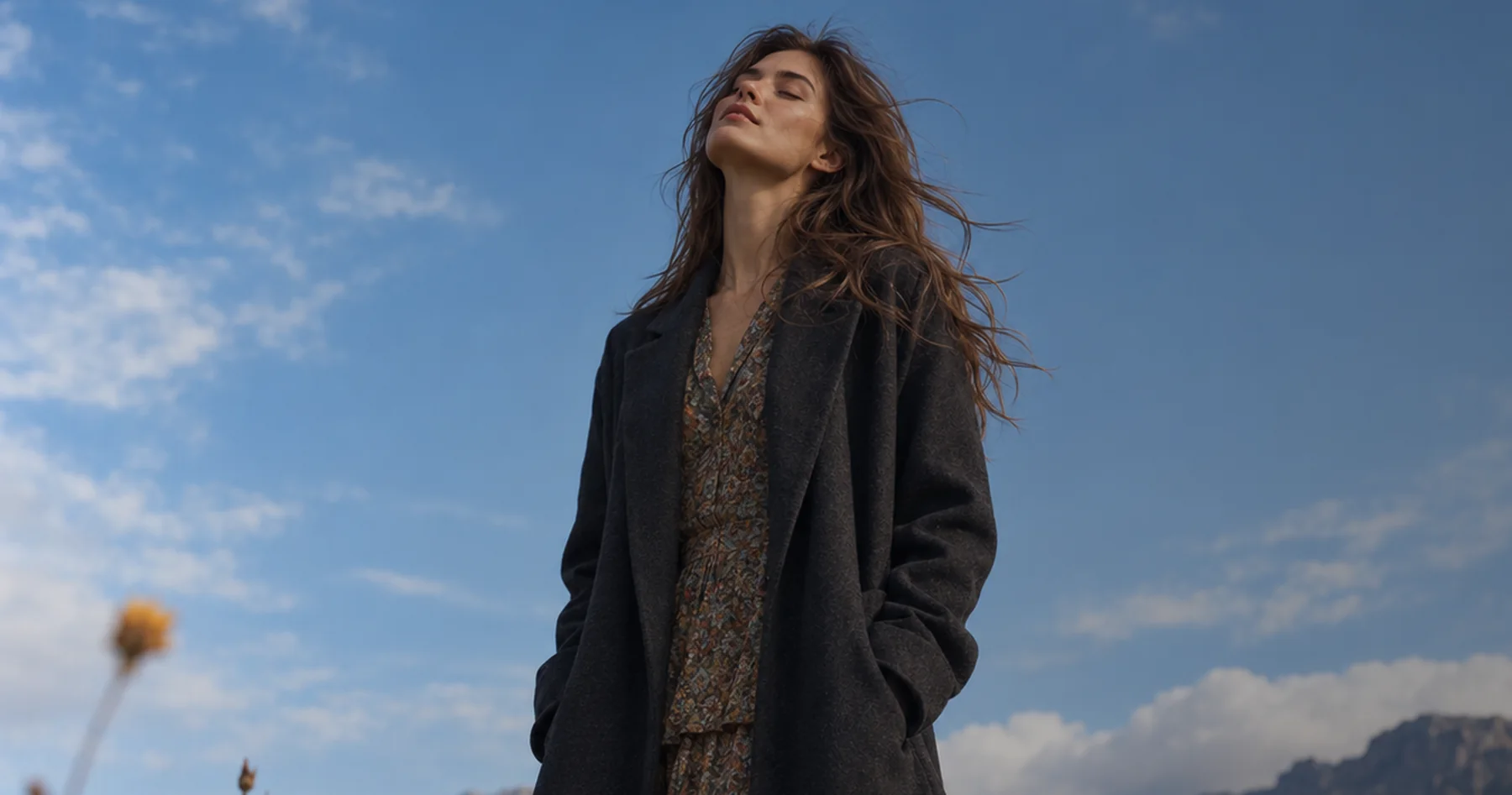 Flux client in a charcoal wool coat over a printed dress, in open country